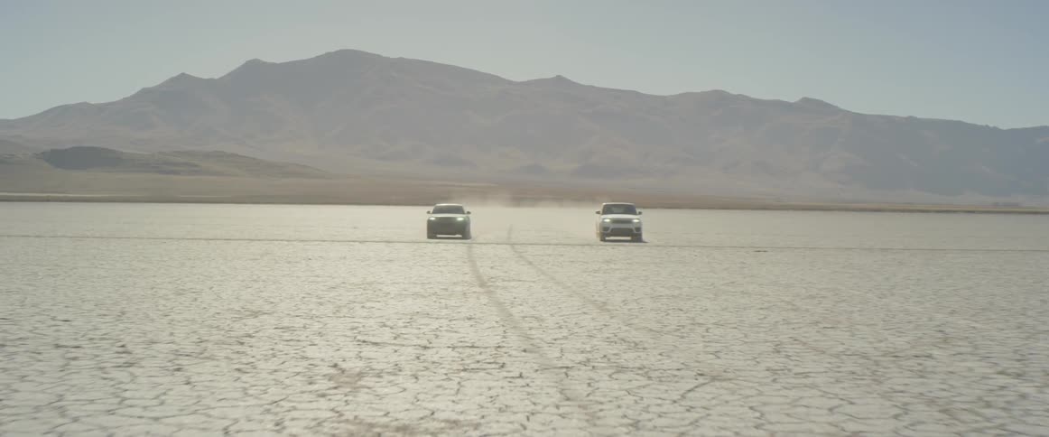 Two range rover sports are approaching at high speed across the salt flats