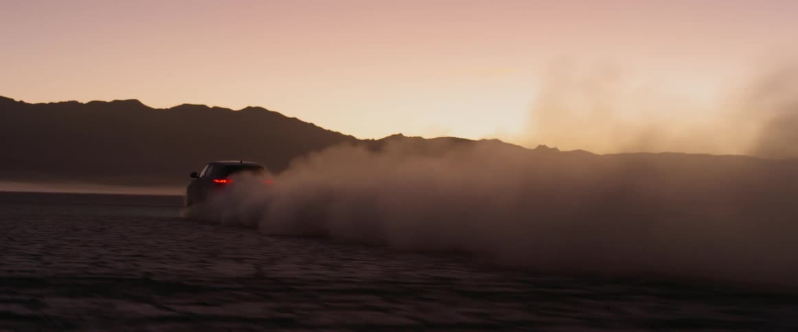 A car races across the desert in a cloud of dust