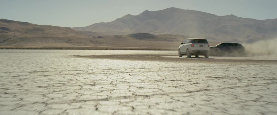 One range rover sport kicks up dust as it circles another on the salt flats
