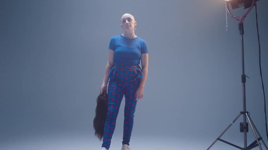 Bald woman posing for a photo shoot holding a long hair wig