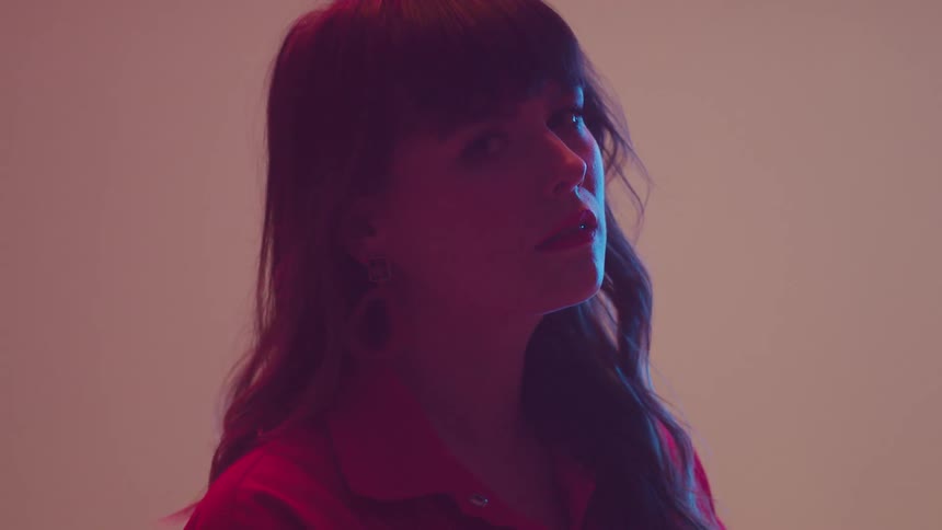 A woman posing under pastel colored lighting