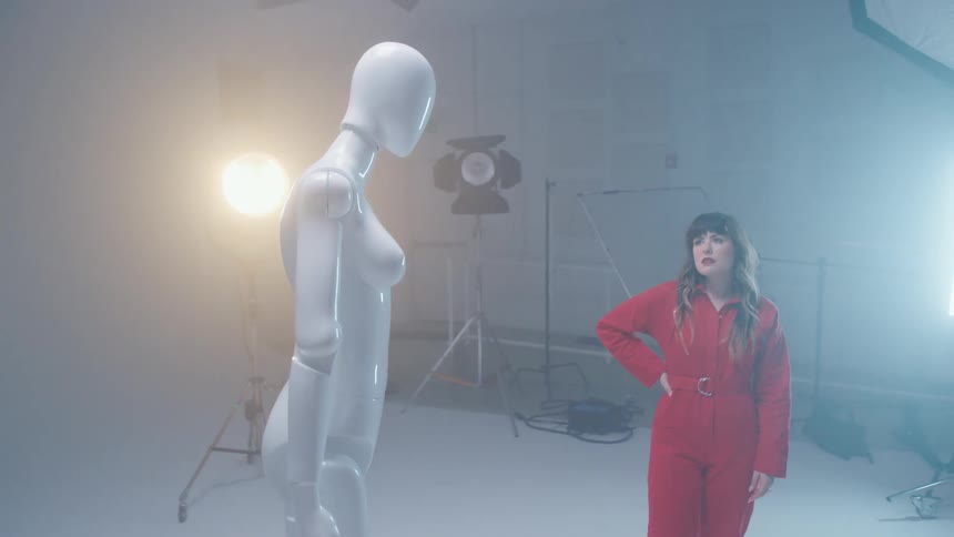 A woman stares at a mannequin in a studio