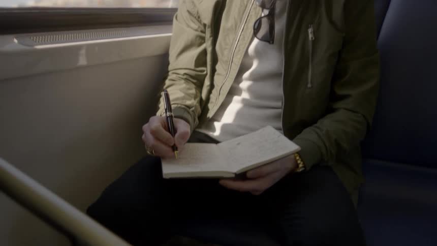 A man writing in a notebook while sitting on a train