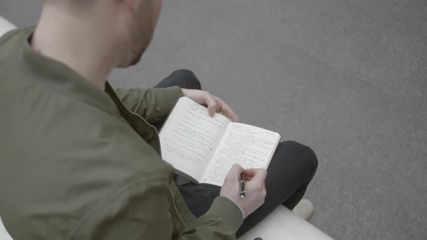 A man sits on a bench and writes in a book