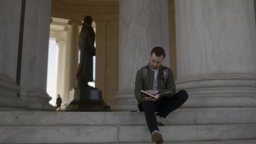 A man sitting at a monument reading a book