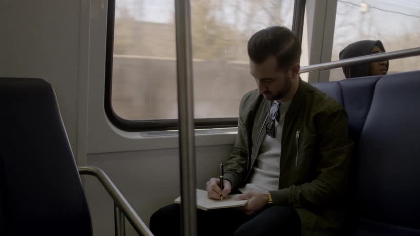 A man sitting on a moving train writes in a journal