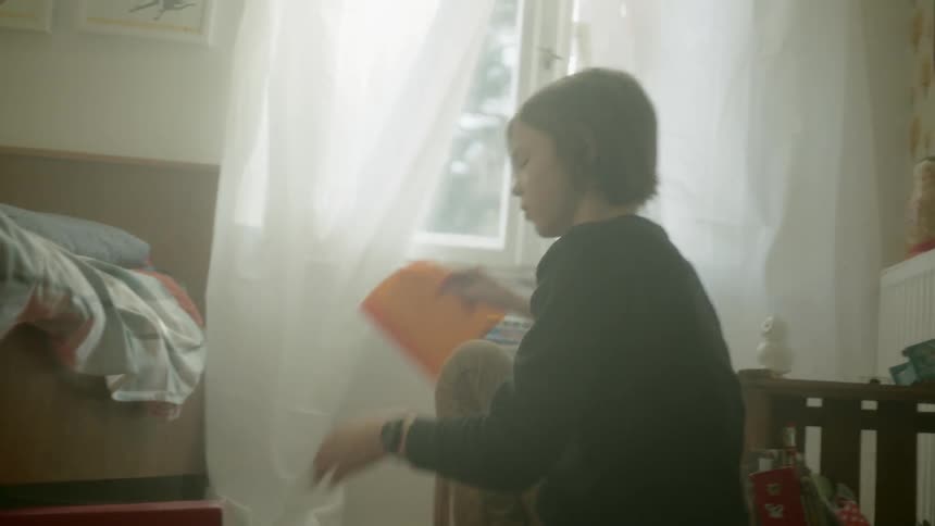 A teen pulls an orange colored transparent film out of an under bed box and holds it up to the window