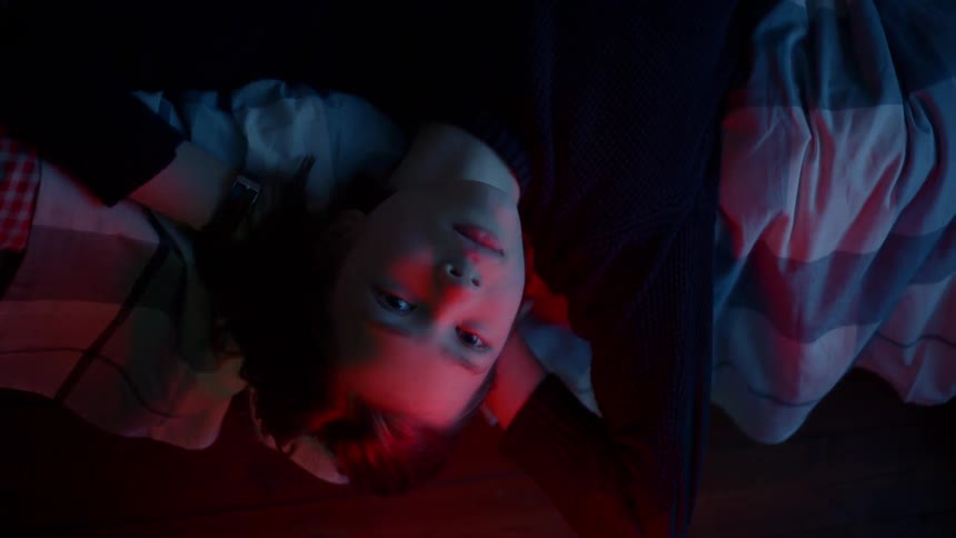 A young boy laying on his back looking straight up at a red light
