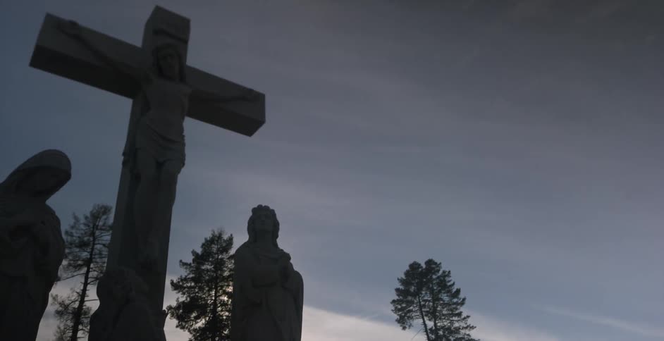 Stone statues of jesus on the cross and other figures outside during sunset