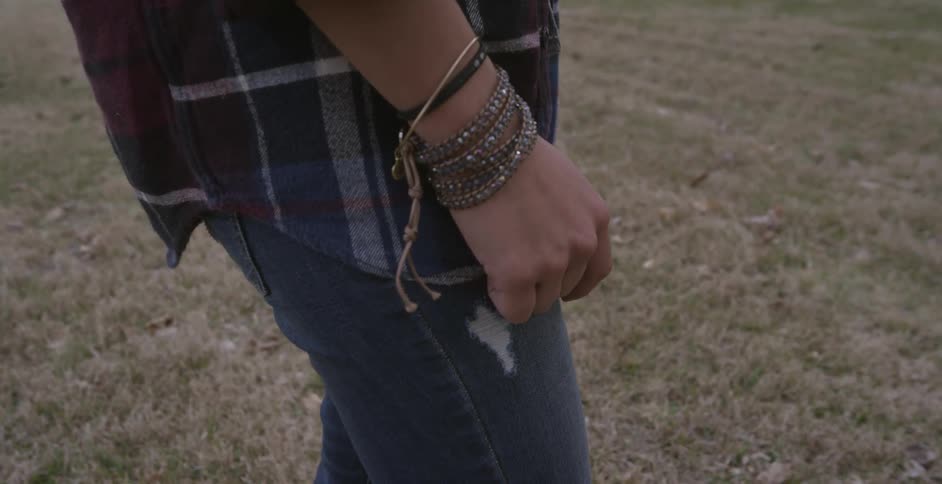 A person wearing bracelets and jeans standing in yellow grass