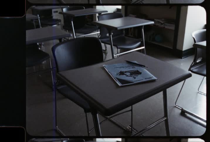 A workbook and pencil sit on a desk in an empty classroom