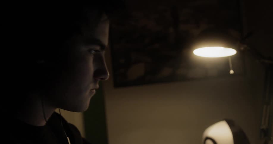 Man sitting at the desk wears the headphones in a dark room