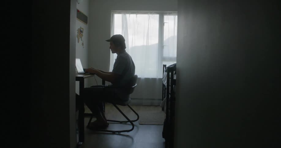 A man is sitting in the room typing at his laptop