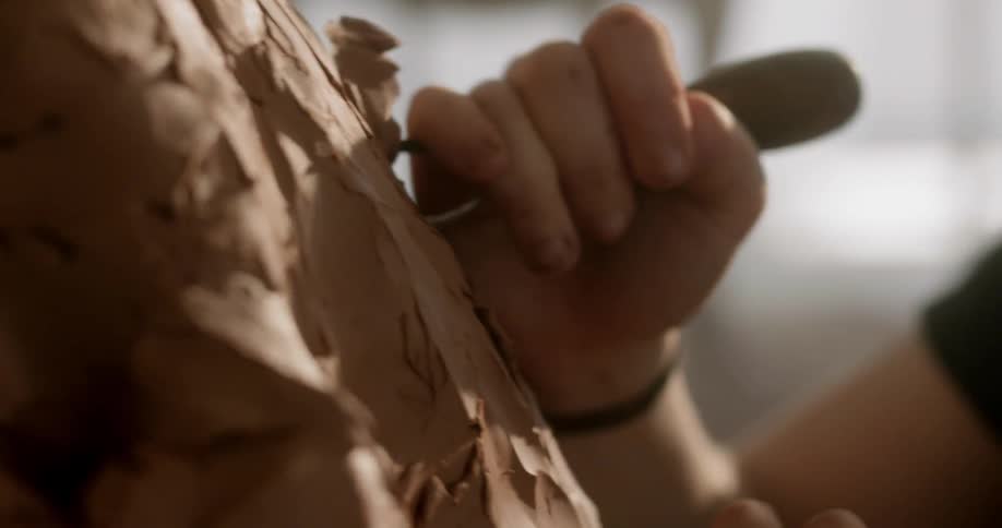 Woman shapes large clay shape with tool