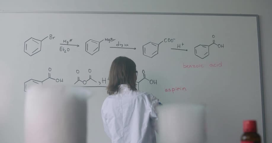 A woman is writing science equations on the board