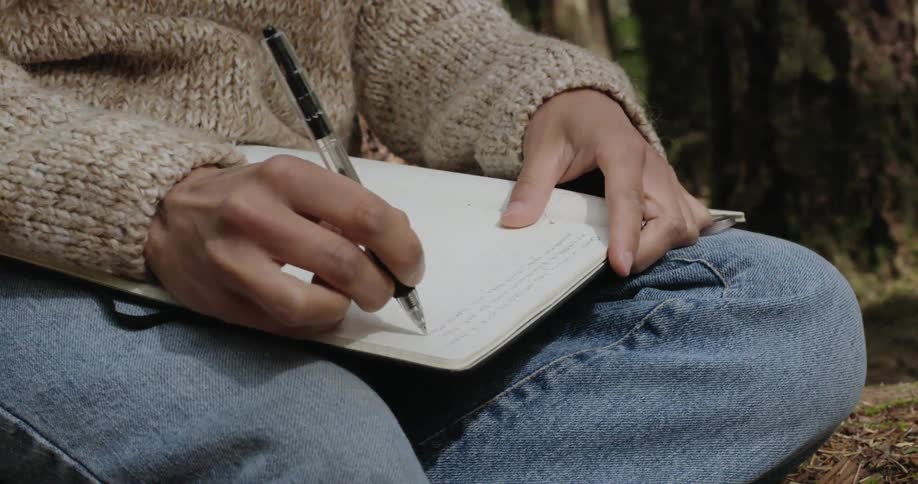 A woman is writing in a journal outdoors