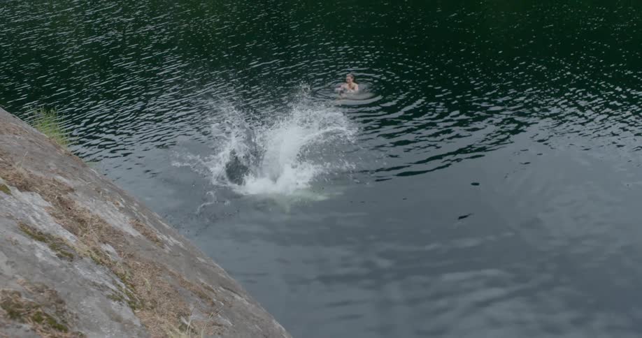 A man jumps from a rock into a lake as he is cheered on by his friends