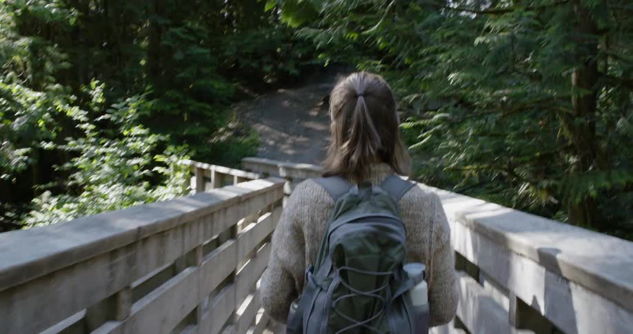 A woman hikes across a narrow pedestrian bridge