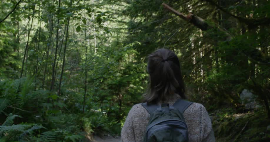 A young woman wearing a backpack walks along a trail through a dense forest