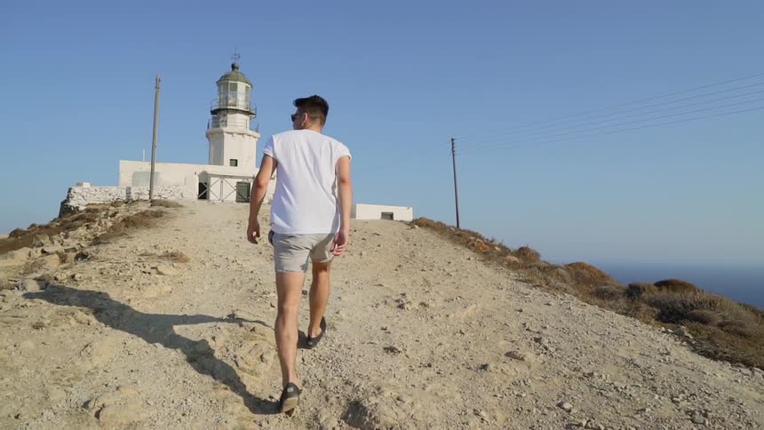 Man walks up sanding incline toward lighthouse