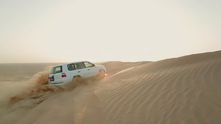 A vehicle drives around a large sand dune