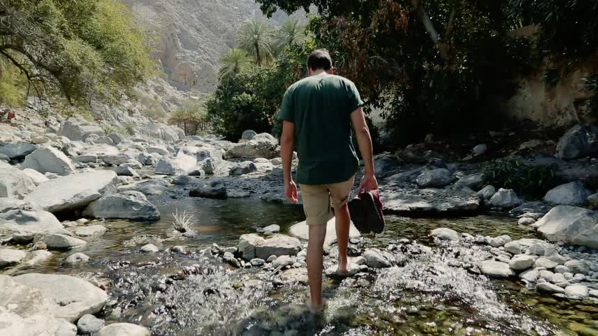 Man walks barefoot through the stony creek in the woods