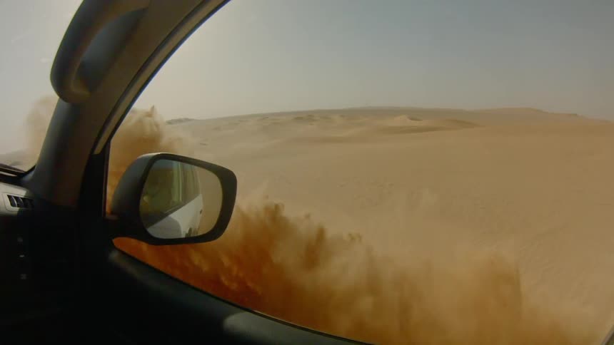 Sand is being tossed into the air as a vehicle drives off road through a desert landscape