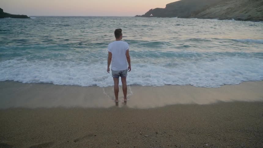 Man stands and looks at the ocean and bay on the beach at dusk