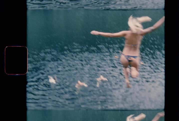 A young blonde woman jumps off a high cliff into a lake