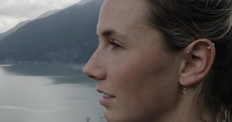 Woman stands near ocean with mountain on horizon looking out