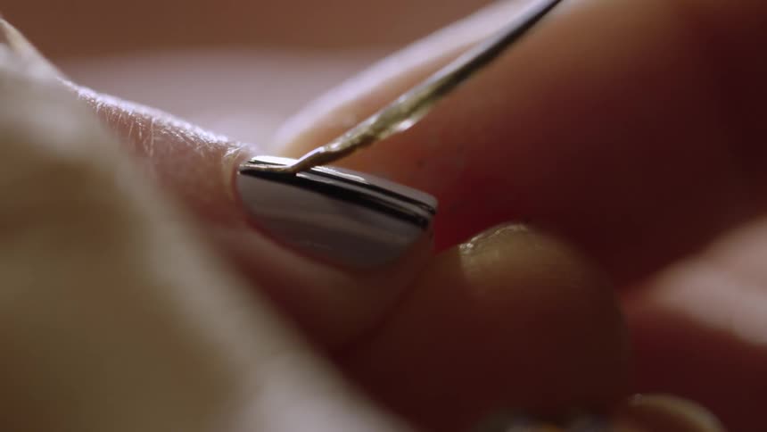 A woman's nail being painted with a white stripe over the middle of a black stripe on a grey nail