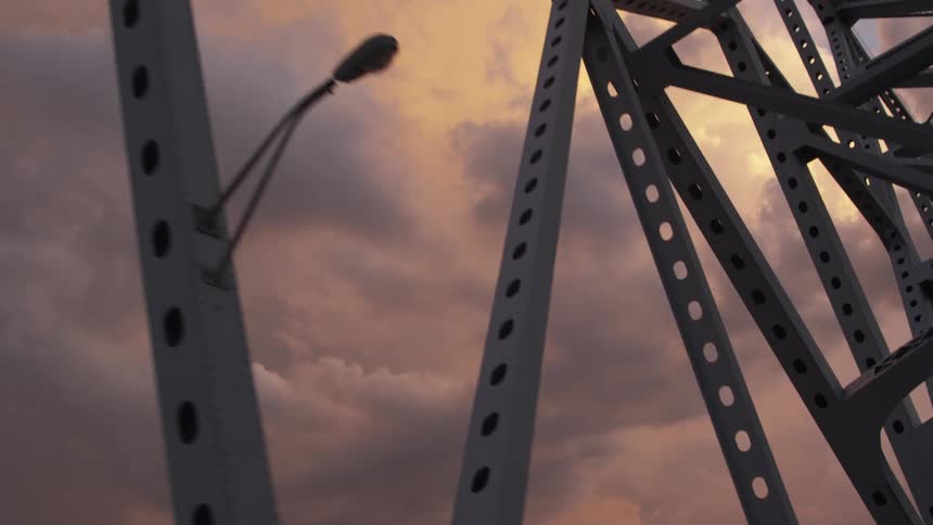 A large metal bridge in front of a very cloudy sky at sunset