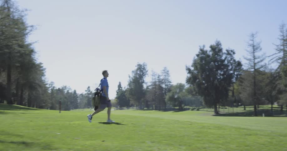 A white male golfer is carrying his golf bag and clubs to the next hold on a golf course