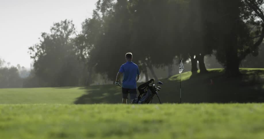 A man pulls a golf club out of his bag on a course