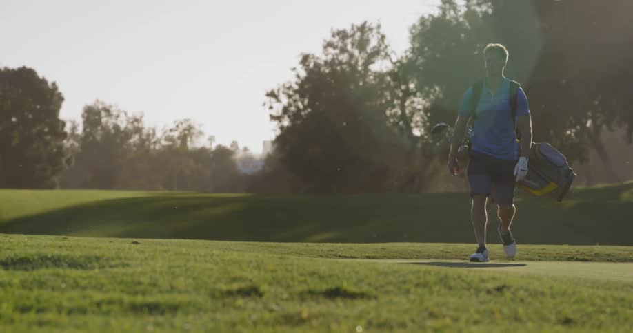 Man walks across golf course carrying golf bag