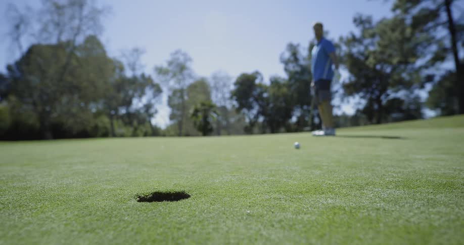 A man hits a golf ball and it rolls past the hole