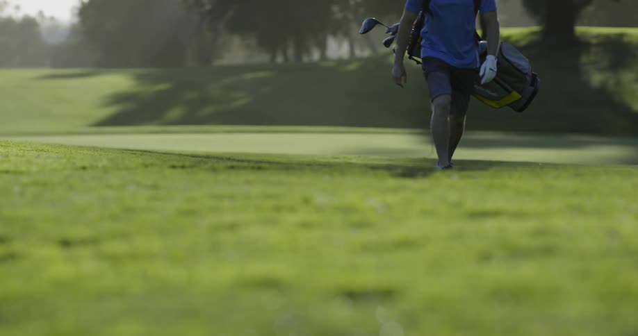 Golfer walks golf course carrying bag full of clubs