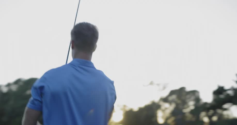 Golf player uses a club to hit the ball into the hole on a course at sunset