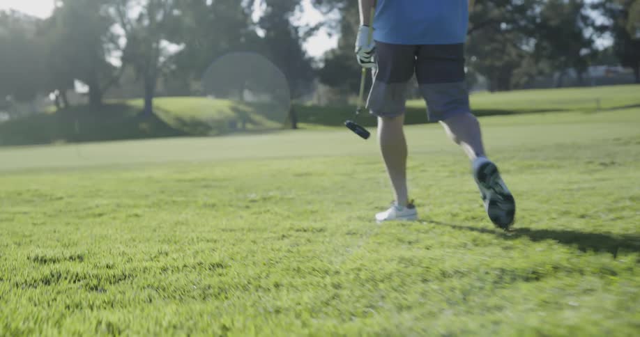 A man carrying a golf club walks across the grass toward the hole
