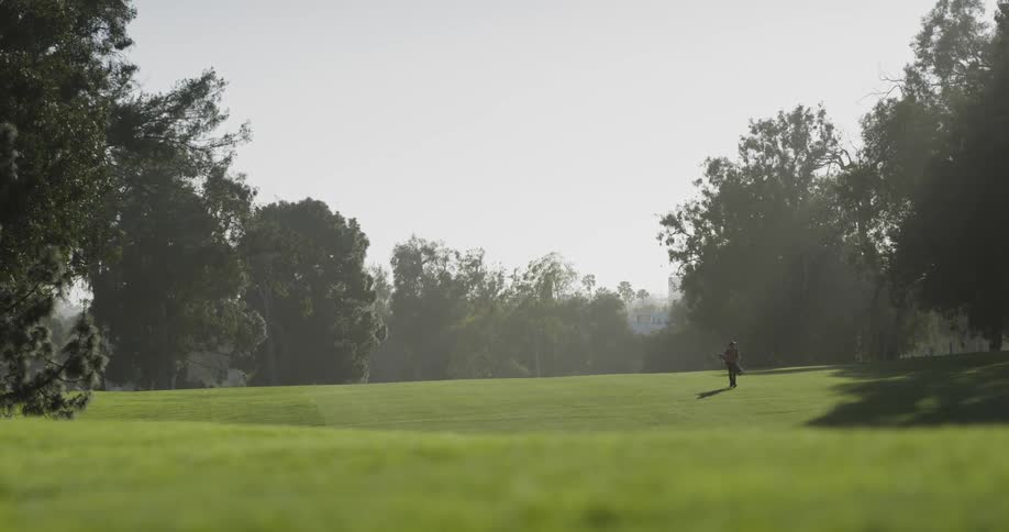 Man walks along a golf course while carrying a bag of golf clubs