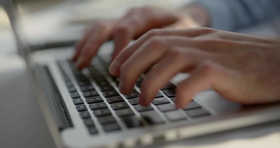 Man sitting at the desk types on laptop in a room