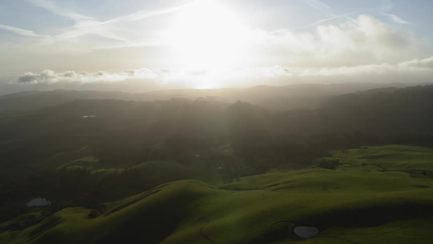 The sun is rising above the green hills