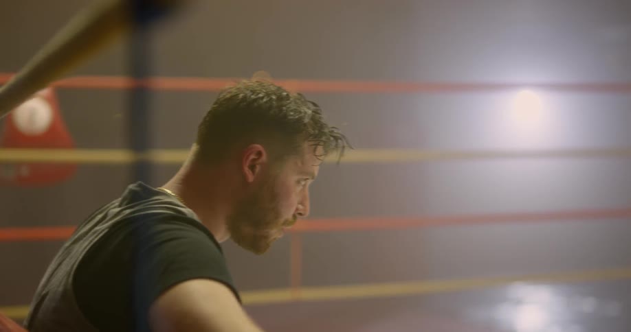 A man sitting on the floor of a boxing ring holding on to the ropes before standing and walking away