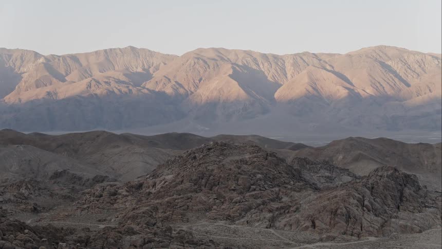 A view of barren mountain range in the far distance with hills during the day