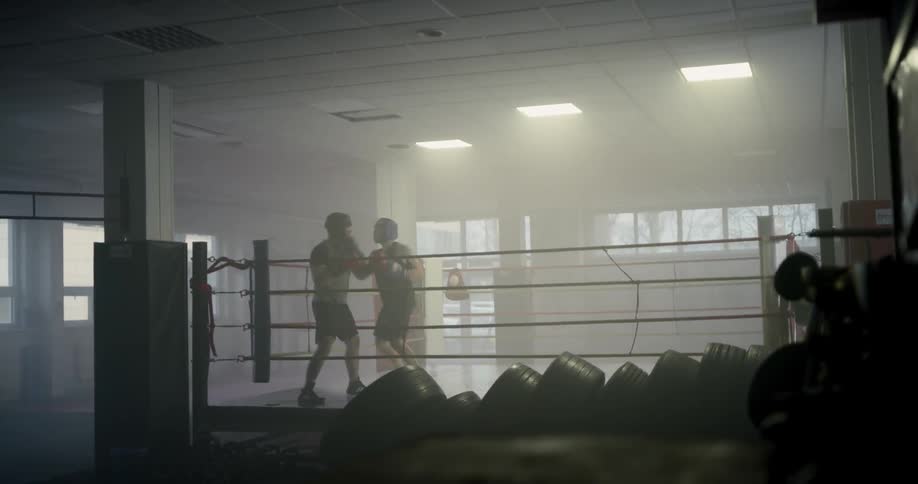 Two boxers spar in the ring in an empty boxing gym