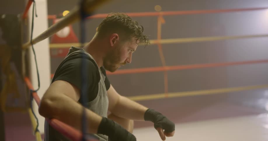 A man sits in a boxing ring and breathes heavily