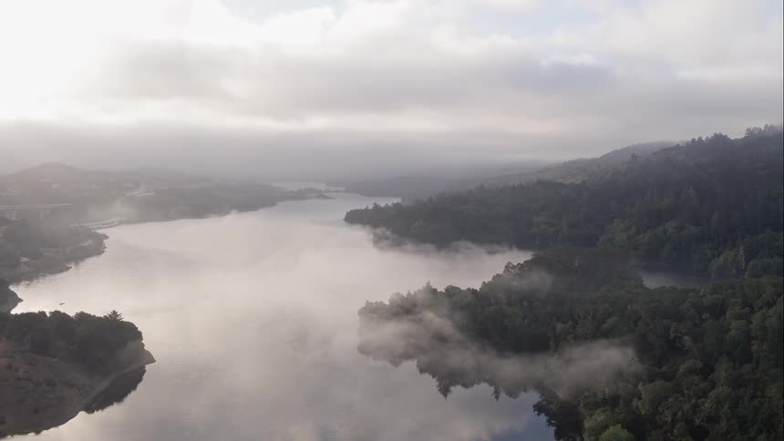 River bordered by forest covered hills reflects the sky