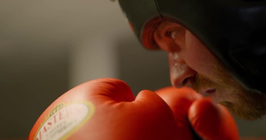 Boxer wearing boxing gloves and a head guard stares at his opponent in the boxing ring