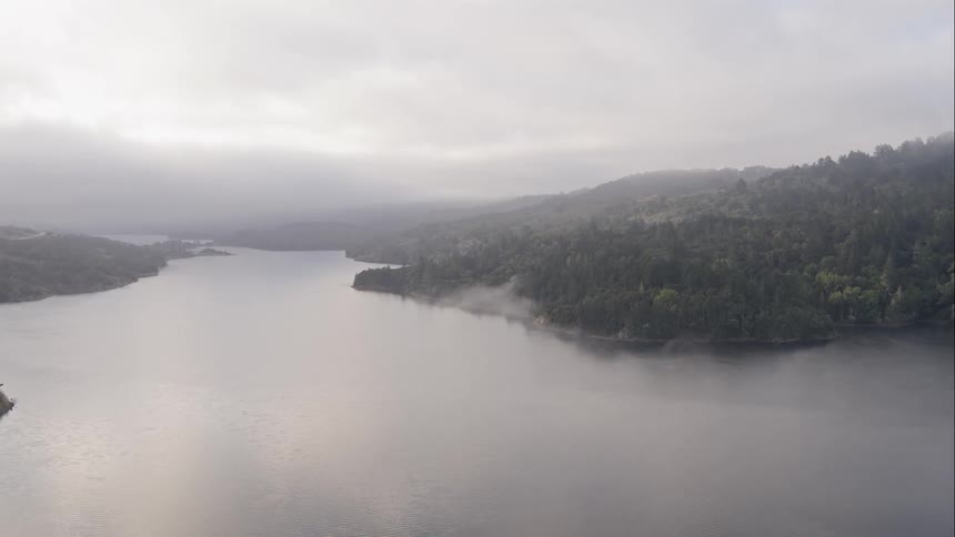 Aerial shot of a lake by a hilly forest