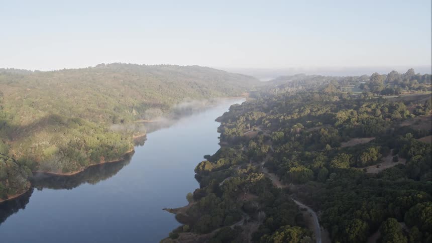 A river flows between two forested hillsides under a blue sky